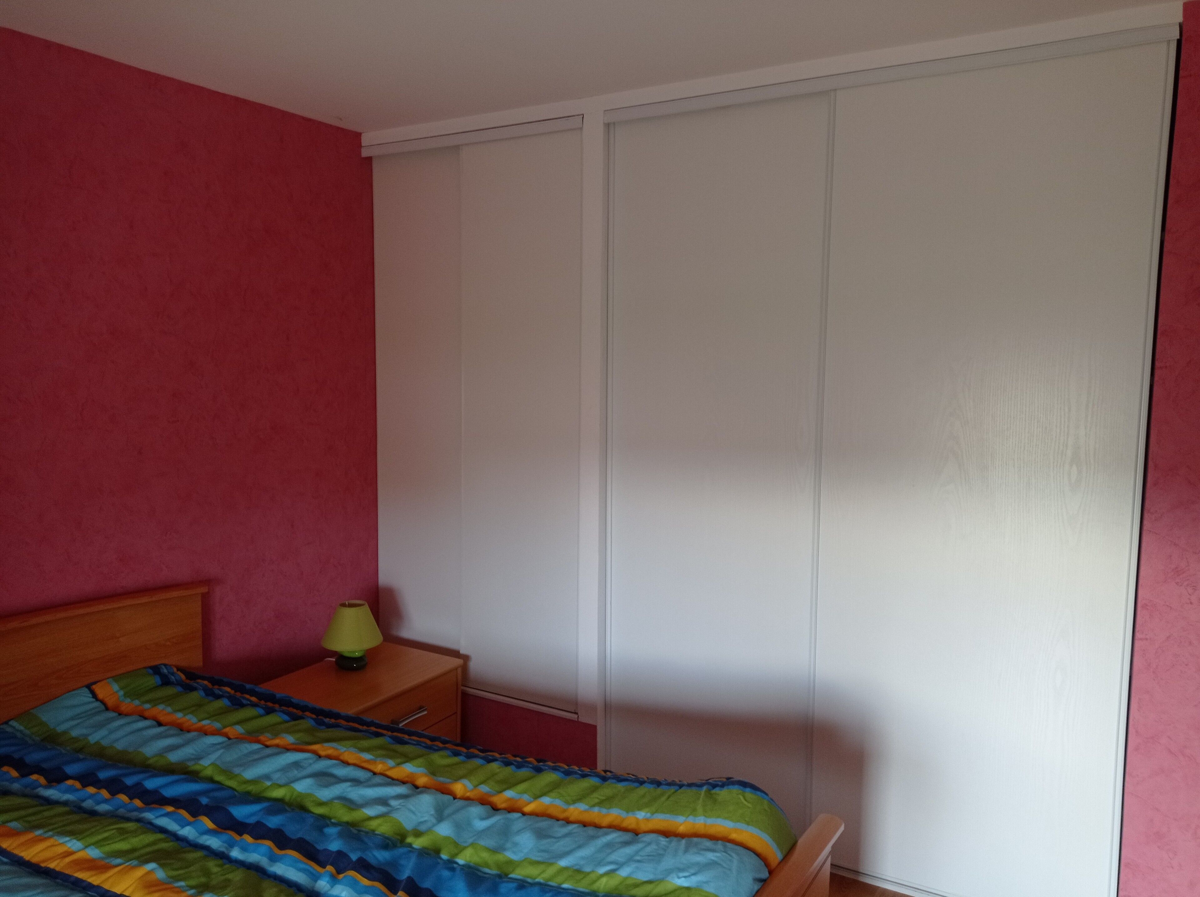 A bedroom with a bed, a nightstand, a lamp, and a wardrobe.
