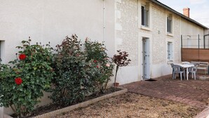A building with a stone facade, a small garden with roses, and a patio area with outdoor furniture.