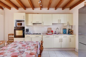 A compact kitchen with a microwave, oven, and sink. There is a dining table with chairs. - Gîte La Chapelière: Private Terrace, Garden & Wi-Fi in Assay, Loire Valley (Assay)