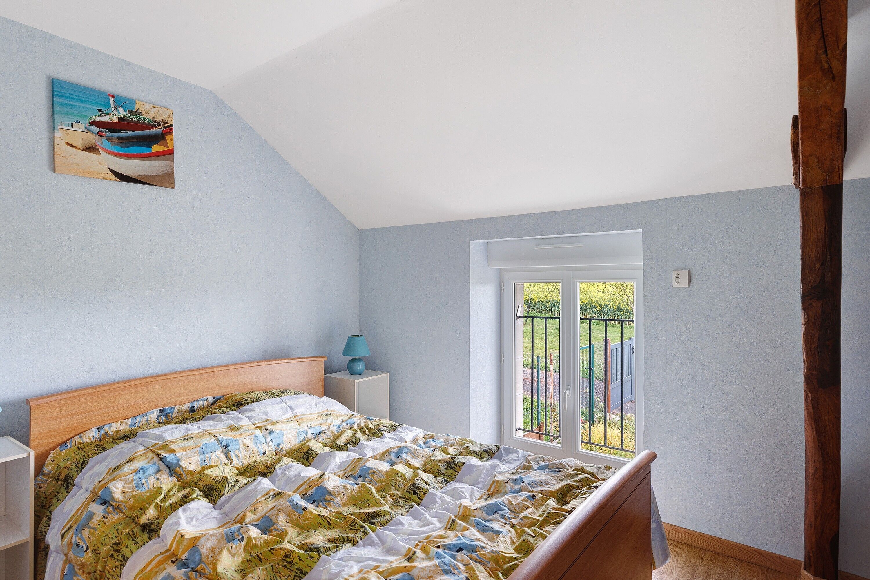Un dormitorio con cama, mesita de noche, lámpara, ventana y puerta que da a un espacio exterior.
