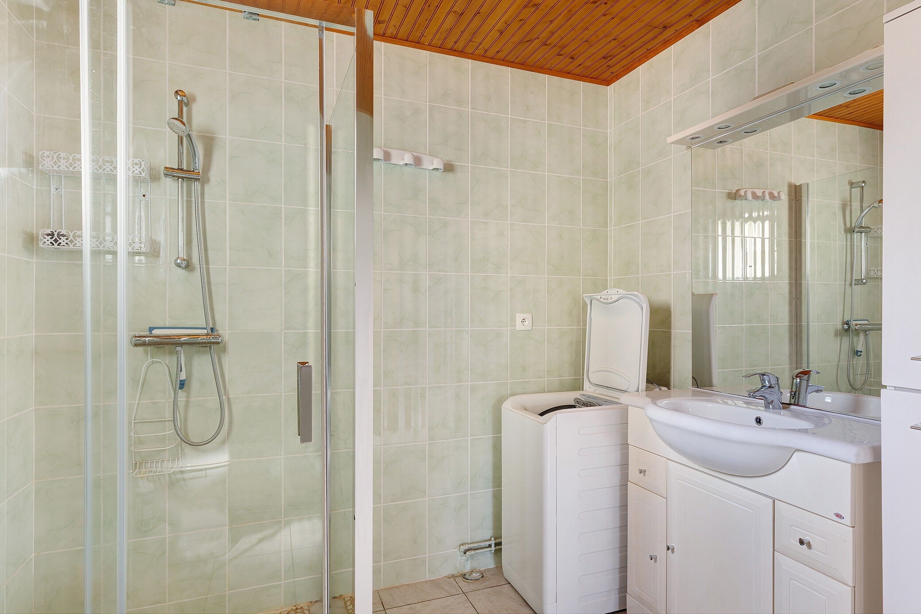 Ein Badezimmer mit Duschkabine aus Glas, einem Waschbecken inklusive Spiegel und einer Toilette.