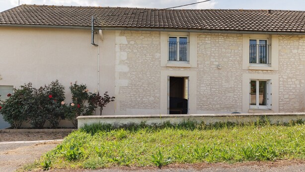 A two-story stone building with a tiled roof, a small entrance, and a garden in front.