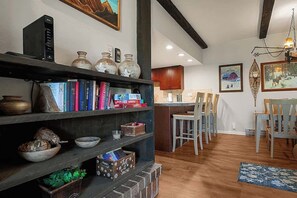 Un salon chaleureux avec une bibliothèque, un coin repas avec des chaises et une cuisine en arrière-plan.