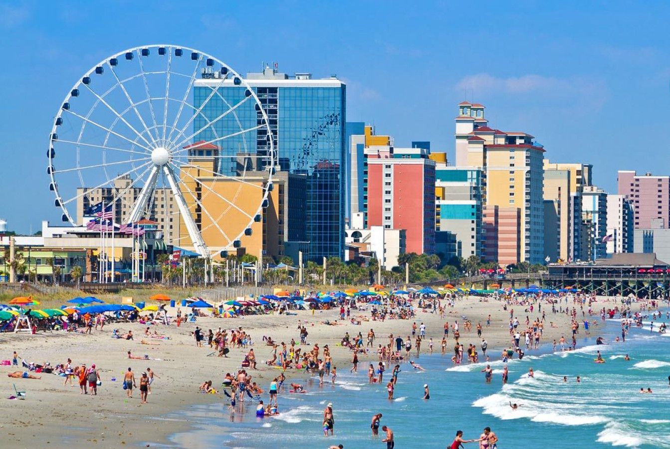 Ein Strand mit einem Riesenrad, ein belebter Strand und eine Skyline mit hohen Gebäuden.