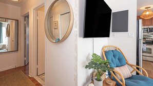 Un intérieur moderne avec un plancher en bois, un miroir rond, un fauteuil bleu rembourré, une plante en pot et un téléviseur à écran plat fixé au mur.
