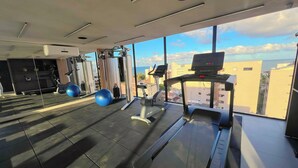 Une salle de sport équipée de matériel d’exercice, d’un tapis de course et d’une grande fenêtre donnant sur la ville.