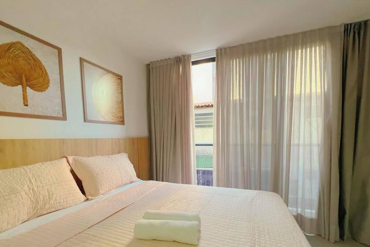 A hotel room with a large bed, a headboard, two framed wall art pieces, and a view through the window.