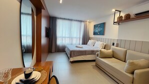 Une chambre d’hôtel comprenant un lit, un canapé, une table à manger avec de l’assiette et des couverts, une télévision et une fenêtre avec des rideaux.