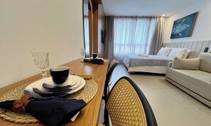 Ett hotellrum med ett matbord dukat för två personer, en säng med ett vitt sänggavel, en soffa och en tavla på väggen.