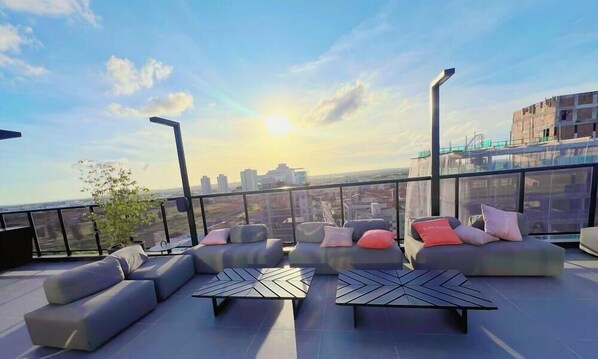 En takterrass med moderna möbler, utsikt över staden och en klar himmel.