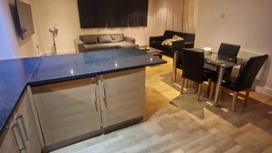 Una cocina moderna con una isla central, comedor con mesa y sillas, y sala de estar con sofá y televisor.