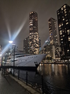A waterfront view with a large yacht docked, tall buildings in the background, and a clear night sky. - Riverthames View Canary Wharf Apartment (London)