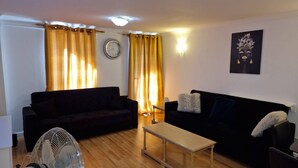 A living room with two sofas, a wooden coffee table, a fan, and a wall clock. - Riverthames View Canary Wharf Apartment (London)