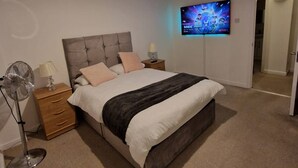 A bedroom with a bed, a TV mounted on the wall, a bedside table, and a floor lamp. - Riverthames View Canary Wharf Apartment (London)