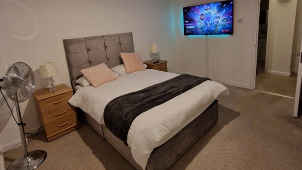A bedroom with a bed, a TV mounted on the wall, a bedside table, and a floor lamp. - Riverthames View Canary Wharf Apartment (London)