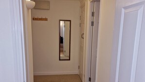 A hallway with carpeted flooring, white walls, a ceiling light, a mirror, and a door. - Riverthames View Canary Wharf Apartment (London)