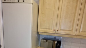 A kitchen with a white refrigerator, a microwave, wooden cabinets, and a tiled floor. - Riverthames View Canary Wharf Apartment (London)