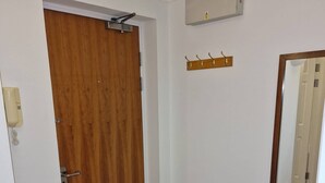 A hallway with a wooden door, a coat hook, a mirror, and a thermostat on the wall. - Riverthames View Canary Wharf Apartment (London)