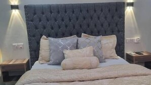 A neatly made bed with a tufted headboard, two bedside tables, and wall-mounted lighting. - Legacy Homes 1B Apartment (Dar es Salaam)