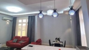 A modern living room with a red sofa, a dining table, and pendant lights. - Legacy Homes 1B Apartment (Dar es Salaam)