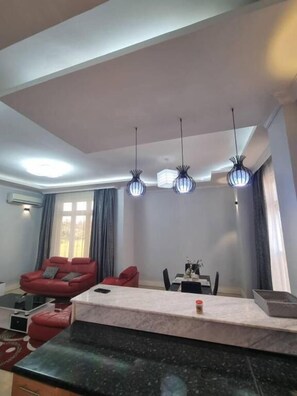 A modern living room with a red sofa, a dining table, and pendant lights. - Legacy Homes 1B Apartment (Dar es Salaam)
