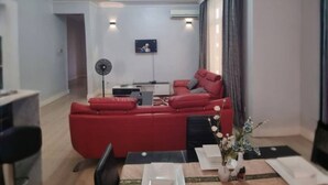 Un salón moderno con un sofá rojo, una mesa de comedor para dos personas y una lámpara de techo.