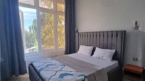 Un dormitorio con una cama grande, una ventana con cortinas, una mesita de noche y vistas a árboles.