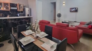 Una sala de estar moderna con comedor, sofás rojos, televisor y cocina con encimeras de mármol.