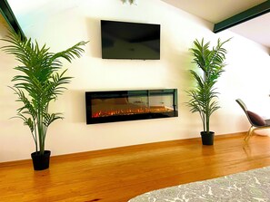 A modern living room with a fireplace, two potted plants, a flat-screen TV, and a wooden floor. - Year-round Private Pool + Jacuzzi • Romantic Villa Setúbal - 25min Lisbon (Setúbal)
