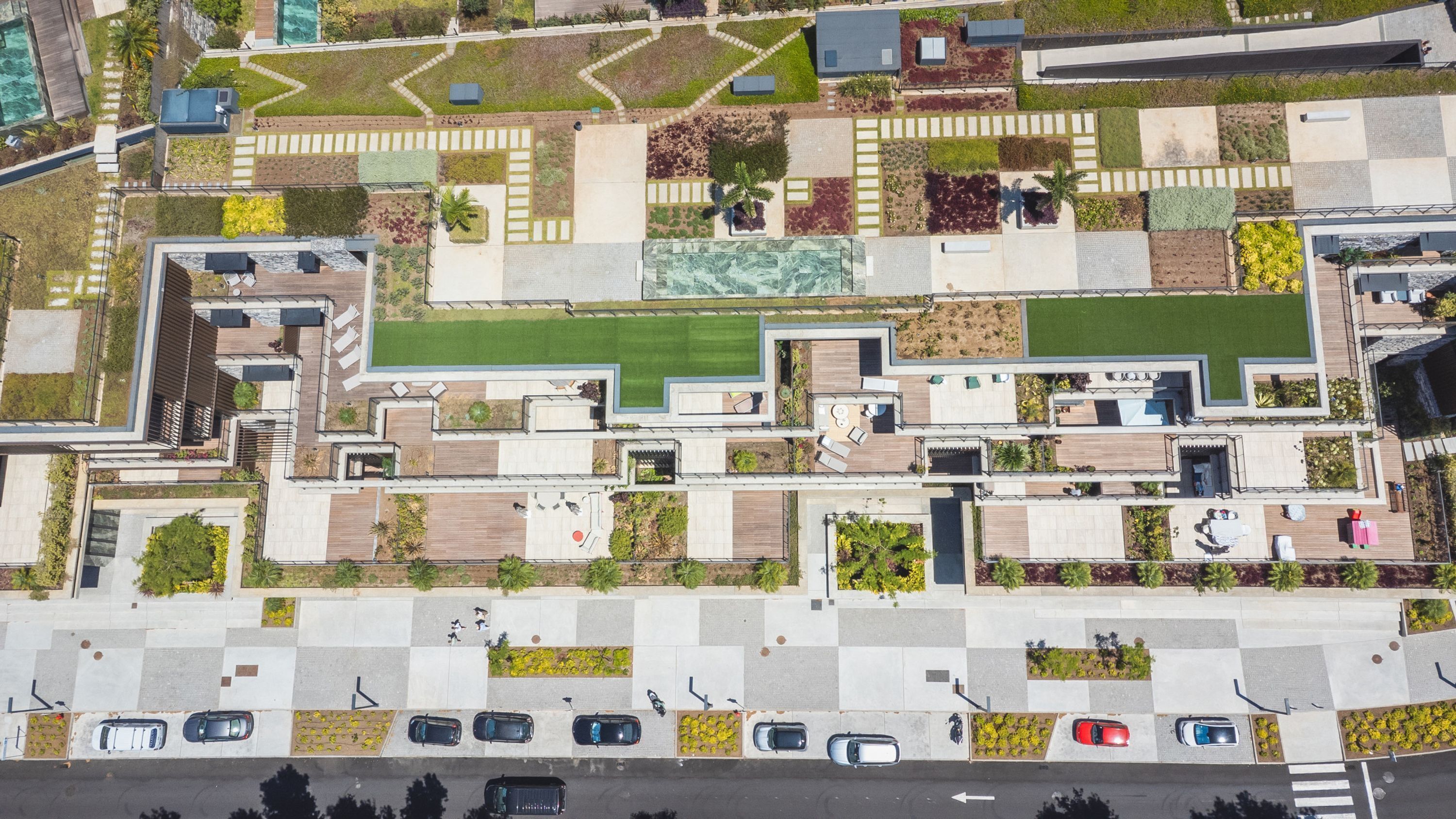 An aerial view of a modern building with multiple floors, featuring a mix of open spaces, balconies, and a central courtyard with a green lawn.