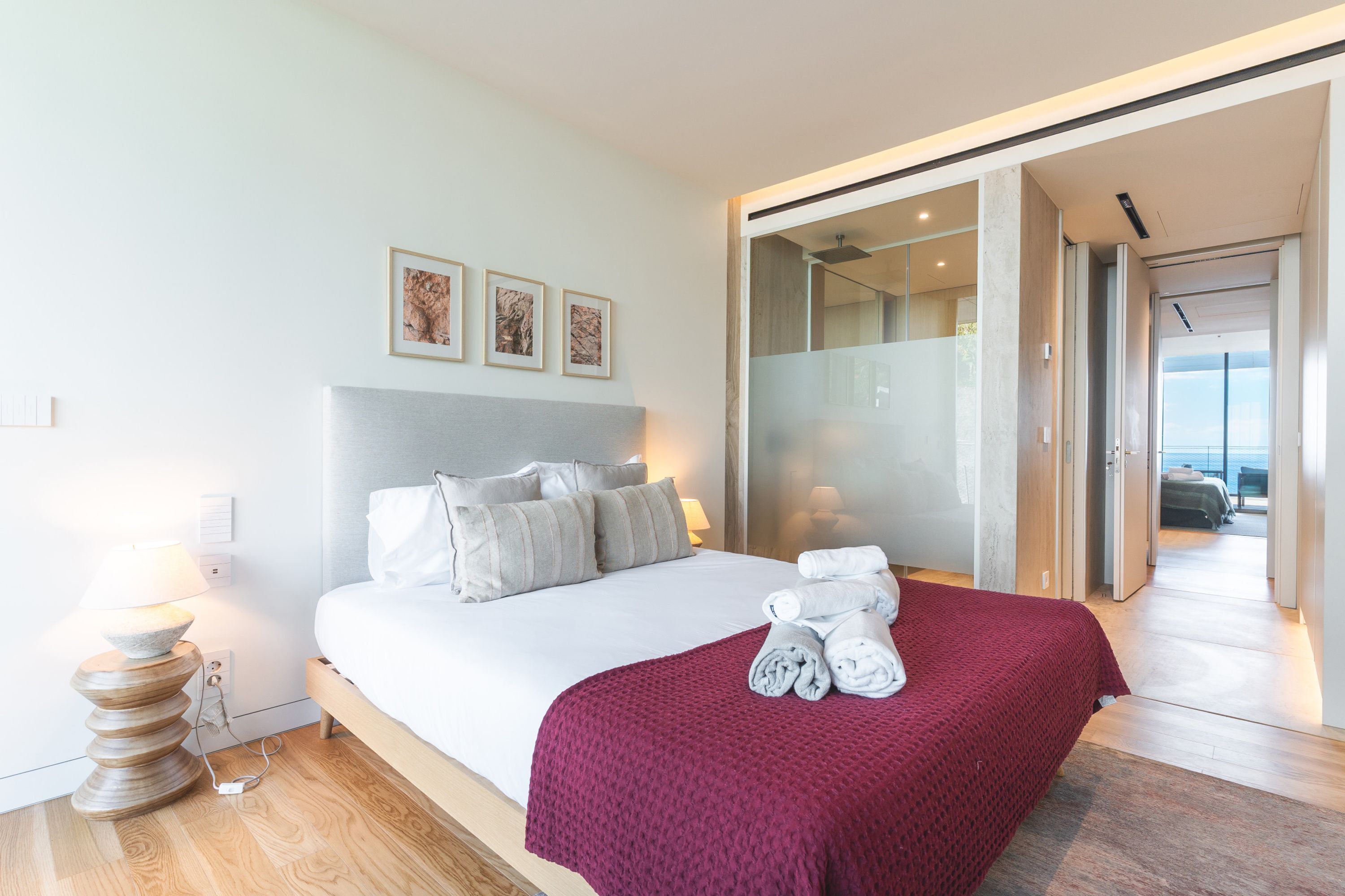 Una camera d'albergo moderna con un letto, una coperta rossa, un tavolino in legno e una lampada a parete.