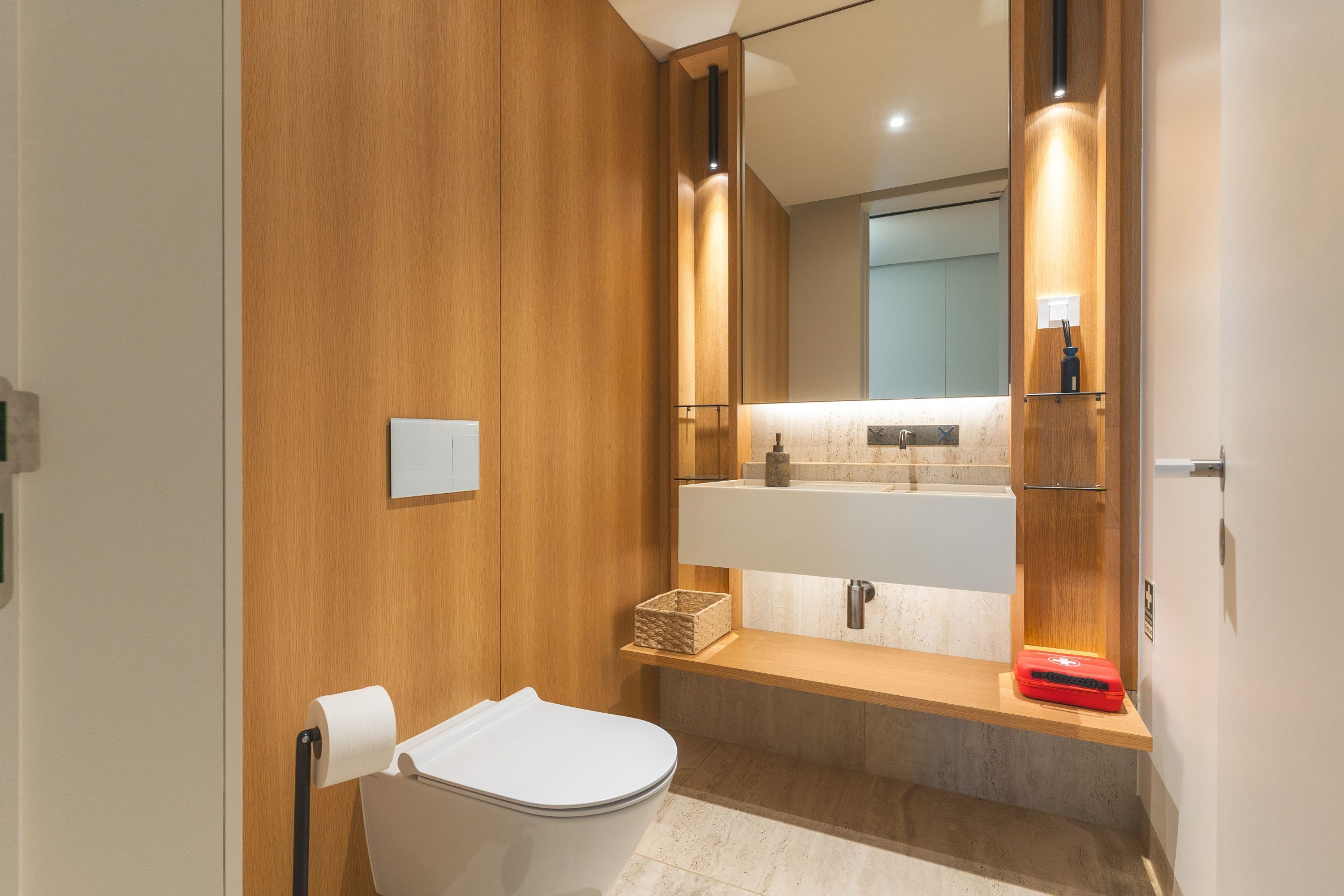 A modern bathroom with a wooden vanity, a white toilet, a mirror, and a sink.