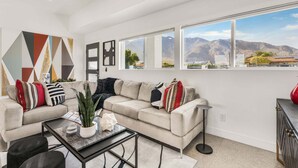 A modern living room with a sectional sofa, a coffee table, and a view of mountains through large windows. - Sunview Escape, a Freshly Remodeled Retreat! (Palm Springs)