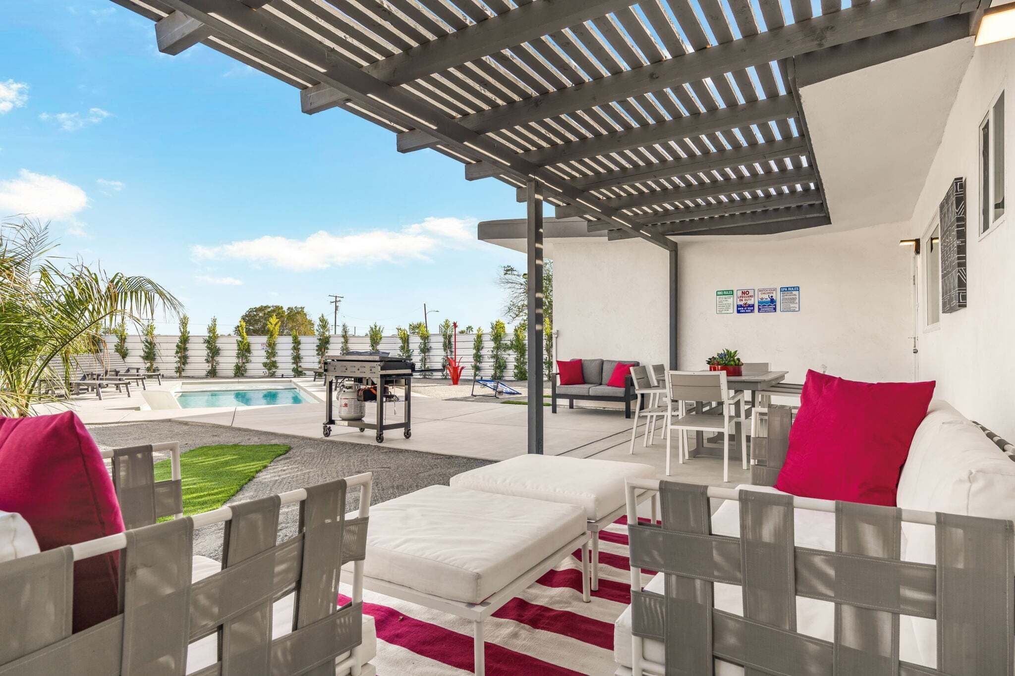 A covered outdoor seating area with a pool, white furniture, and a pergola.