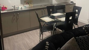 Una cuina moderna amb zona de menjador, amb armaris de tons clars, un fogó negre i una taula de dinar de vidre amb caires.