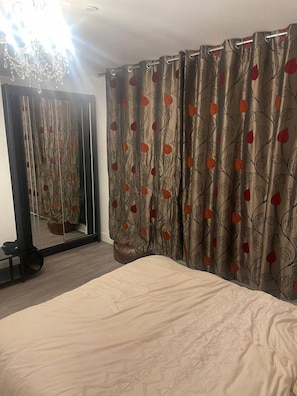 A bedroom with a bed, a mirror, and curtains with a leaf pattern.