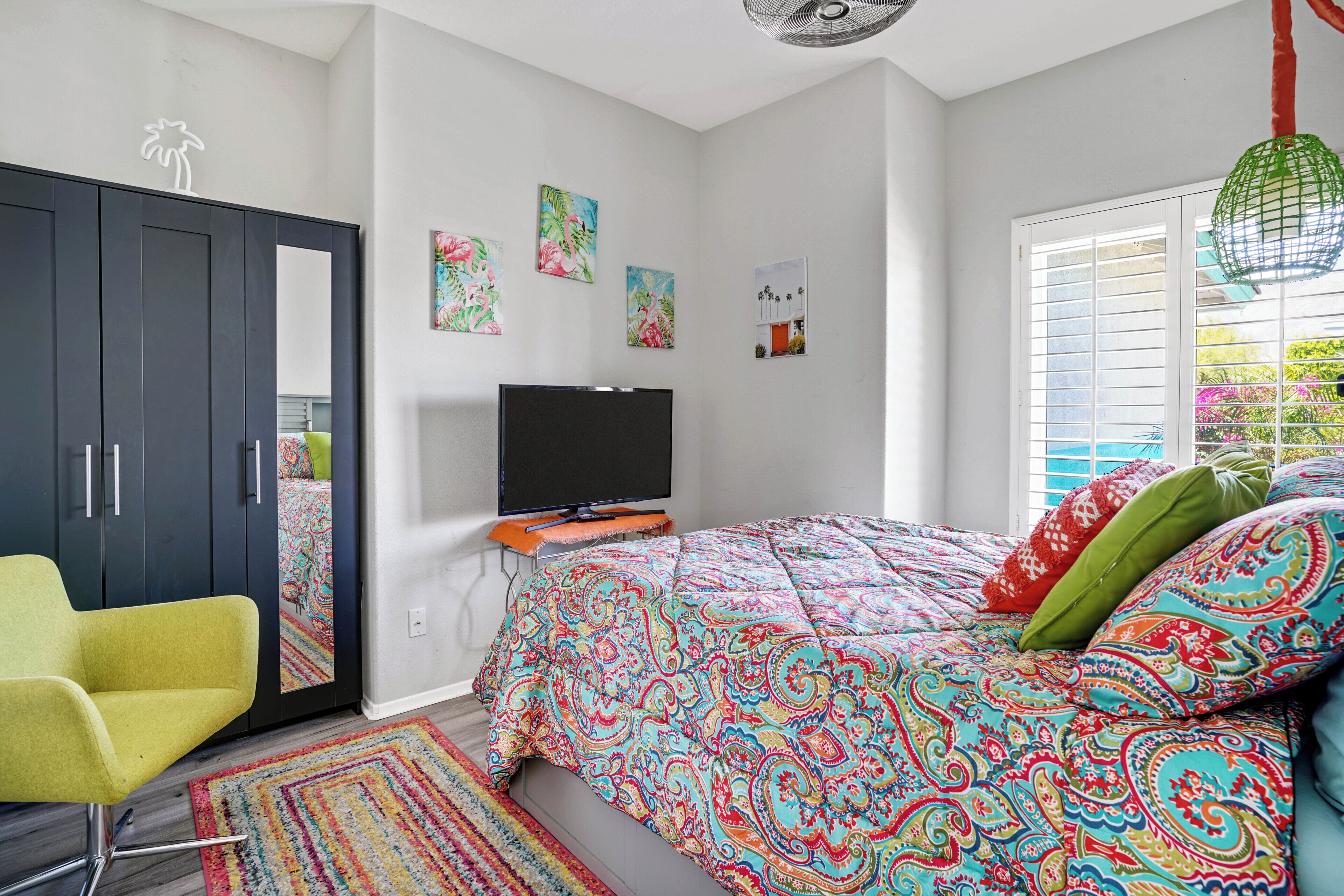 A bedroom with a bed, a TV, a wardrobe, and artwork on the wall.