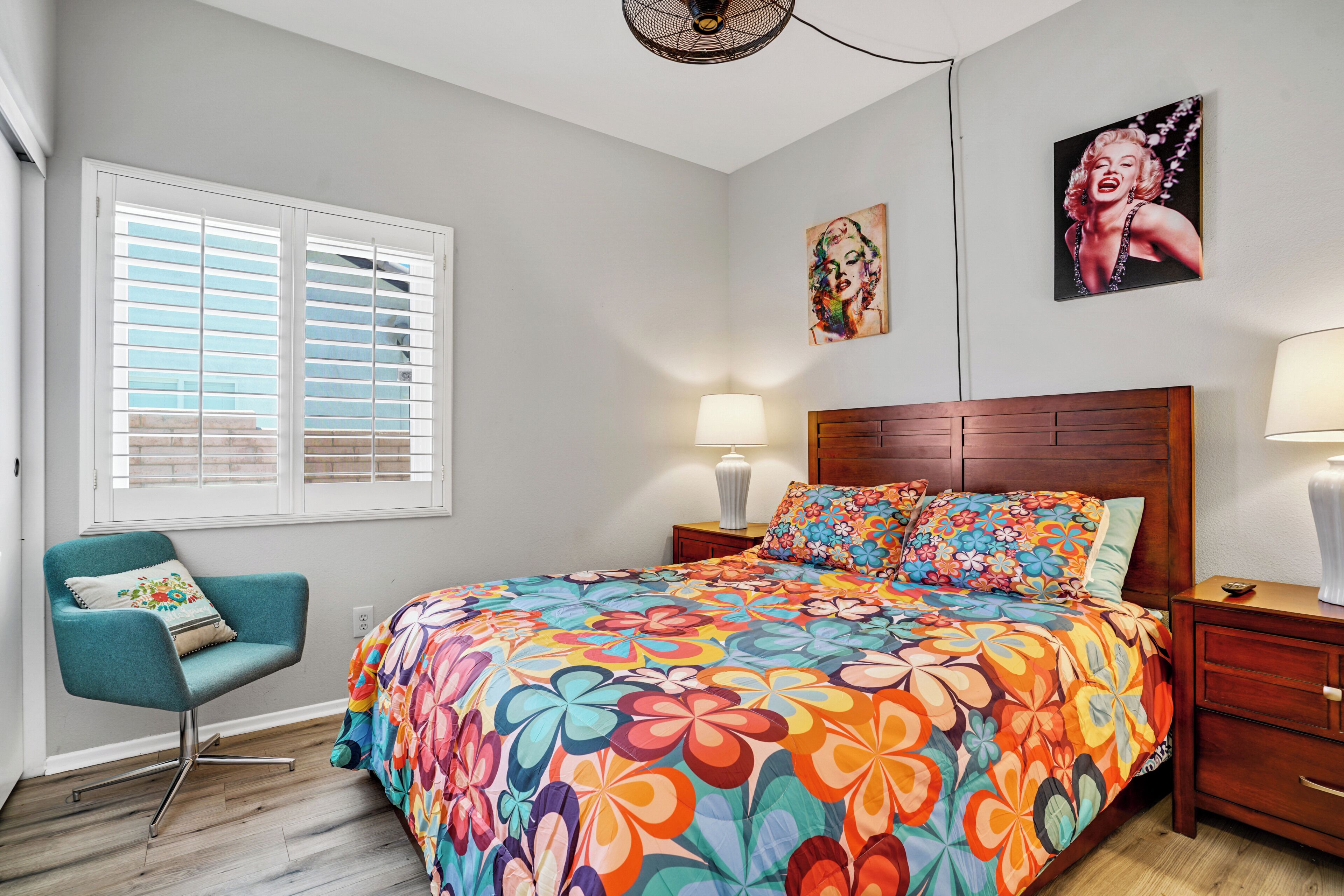 Un dormitorio con colcha estampada, cabecera de madera, un sillón turquesa y dos lámparas de noche.
