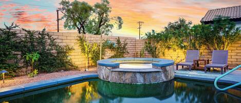 Una piscina con hidromasaje, rodeada por un muro de ladrillo y plantas.