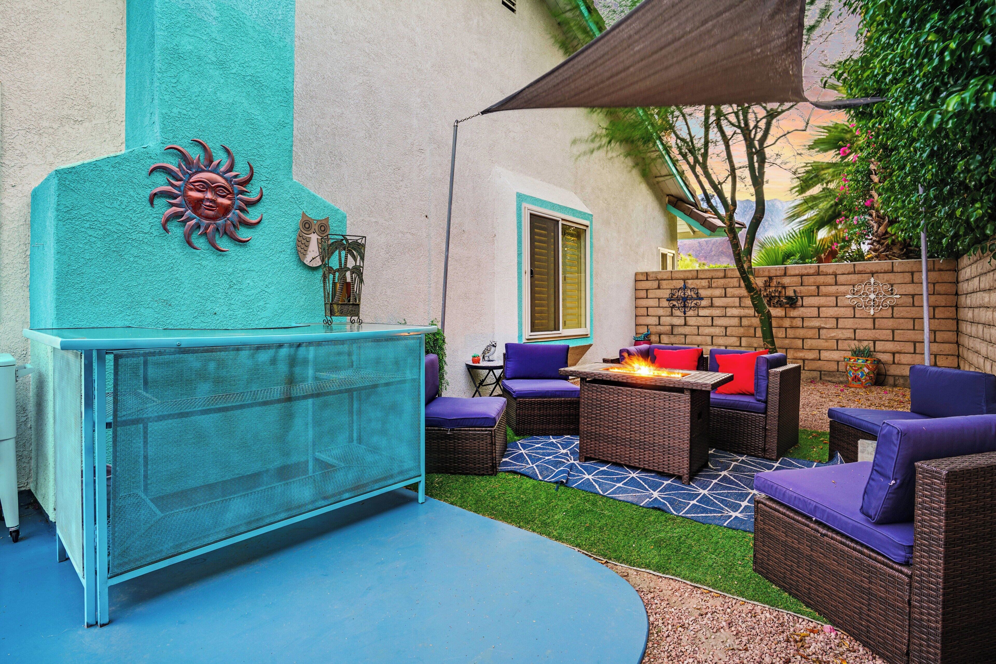Un patio con un conjunto de sofá azul, una mesita con chimenea y una pared decorativa con motivos de sol y lechuzas.