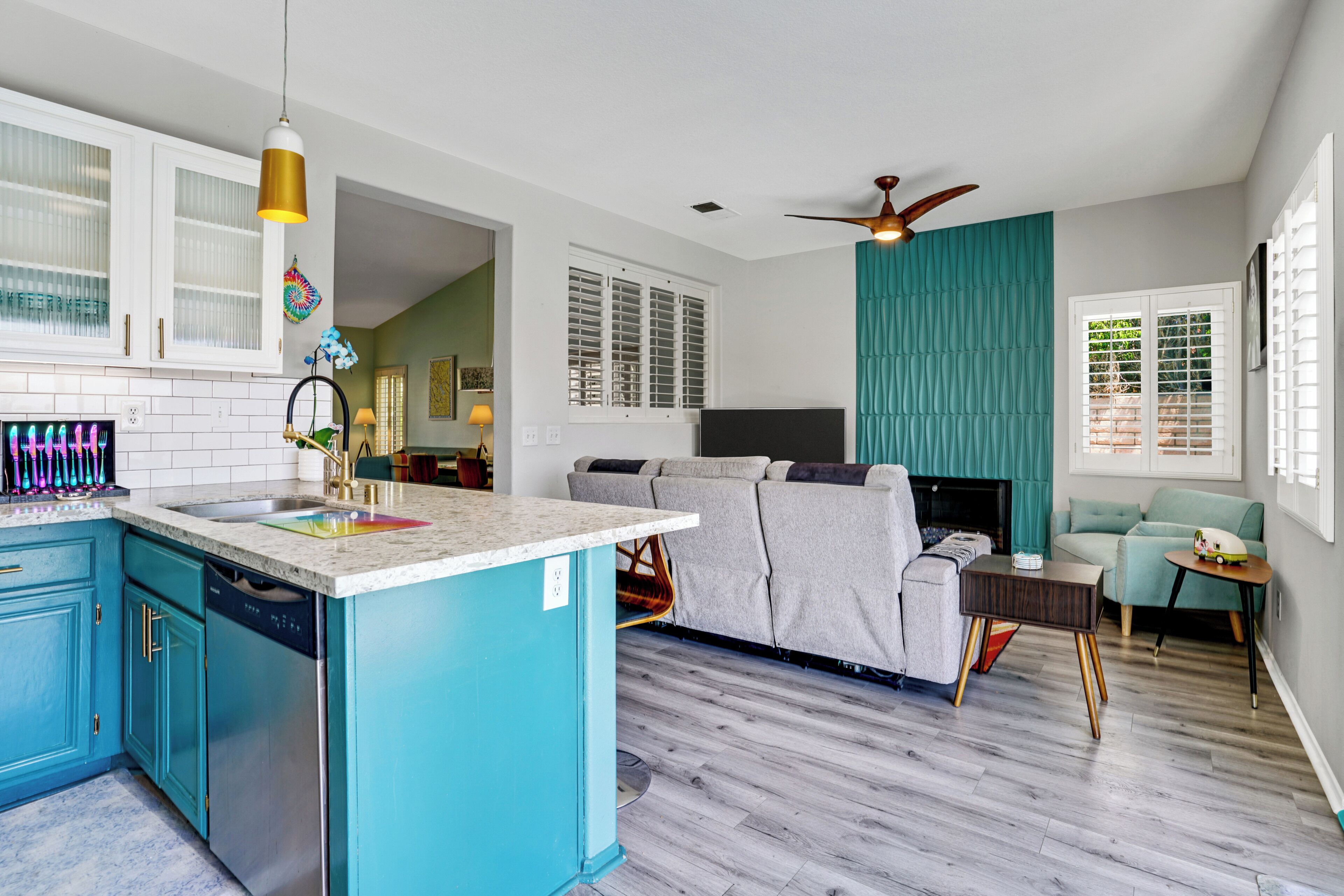 A modern kitchen with a central island, built-in cabinets, and a dishwasher. There is a dining area with a sofa and a small table.