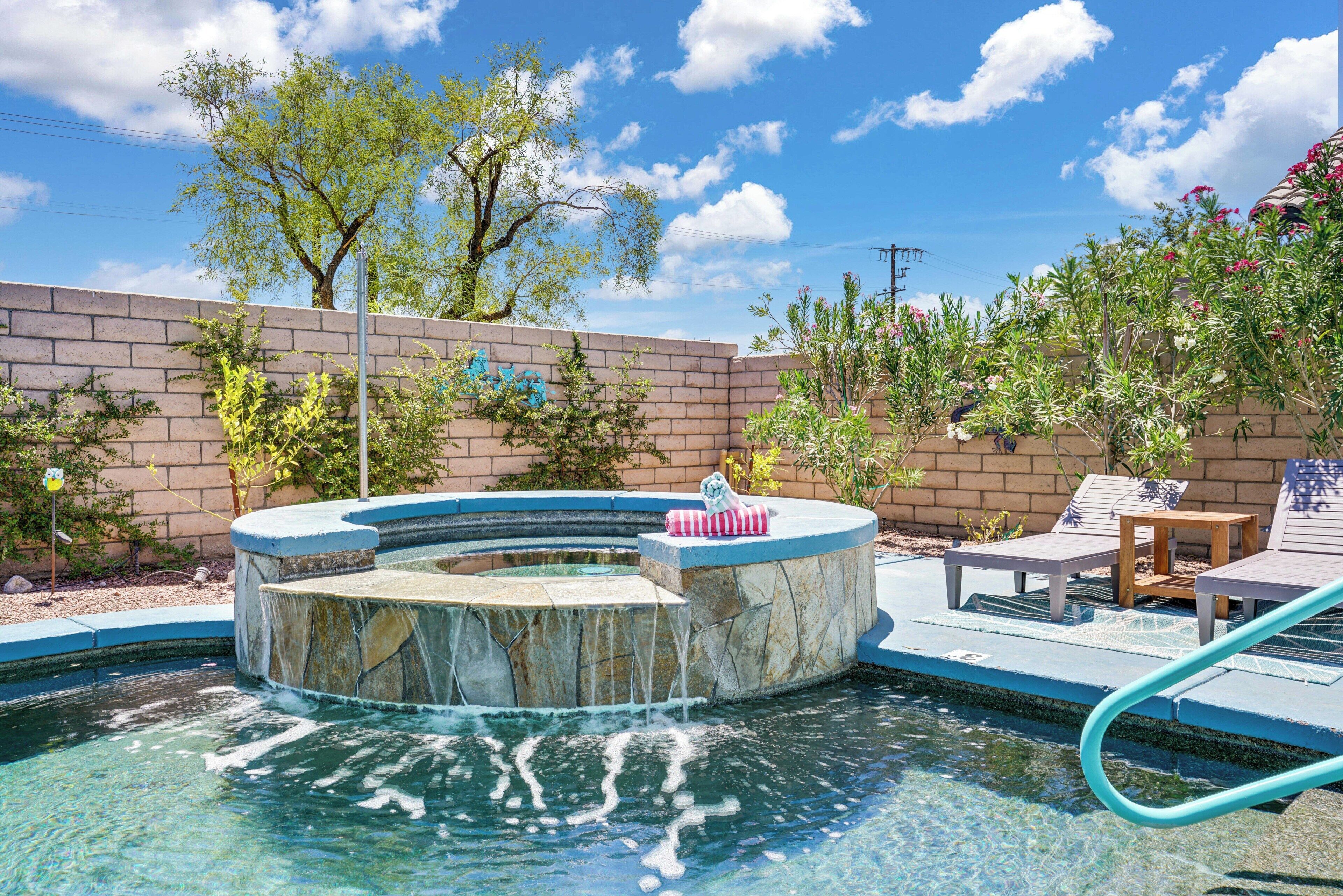 A swimming pool with a hot tub, lounge chairs, and a brick wall.