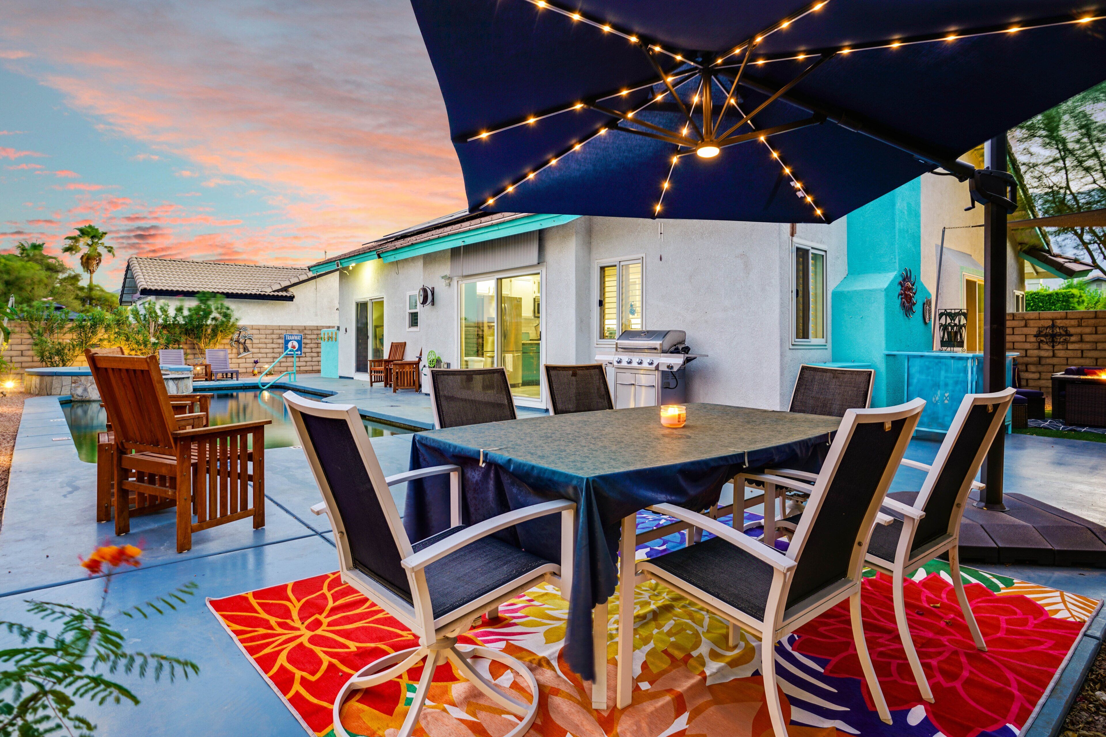 An outdoor patio with a table and chairs, a barbecue grill, and a swimming pool.