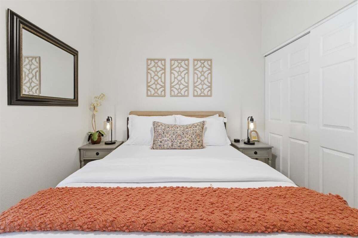A neatly arranged bedroom with a bed, two bedside tables, a mirror, and decorative wall panels.