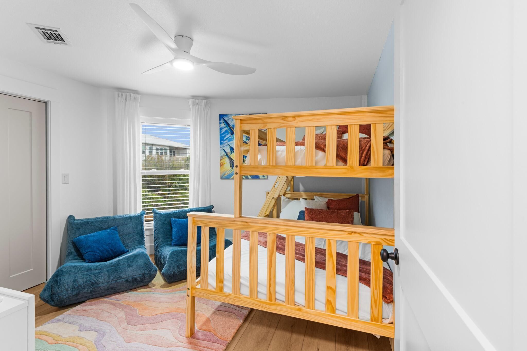 A room with a bunk bed, a blue sofa, a ceiling fan, and a window with curtains.