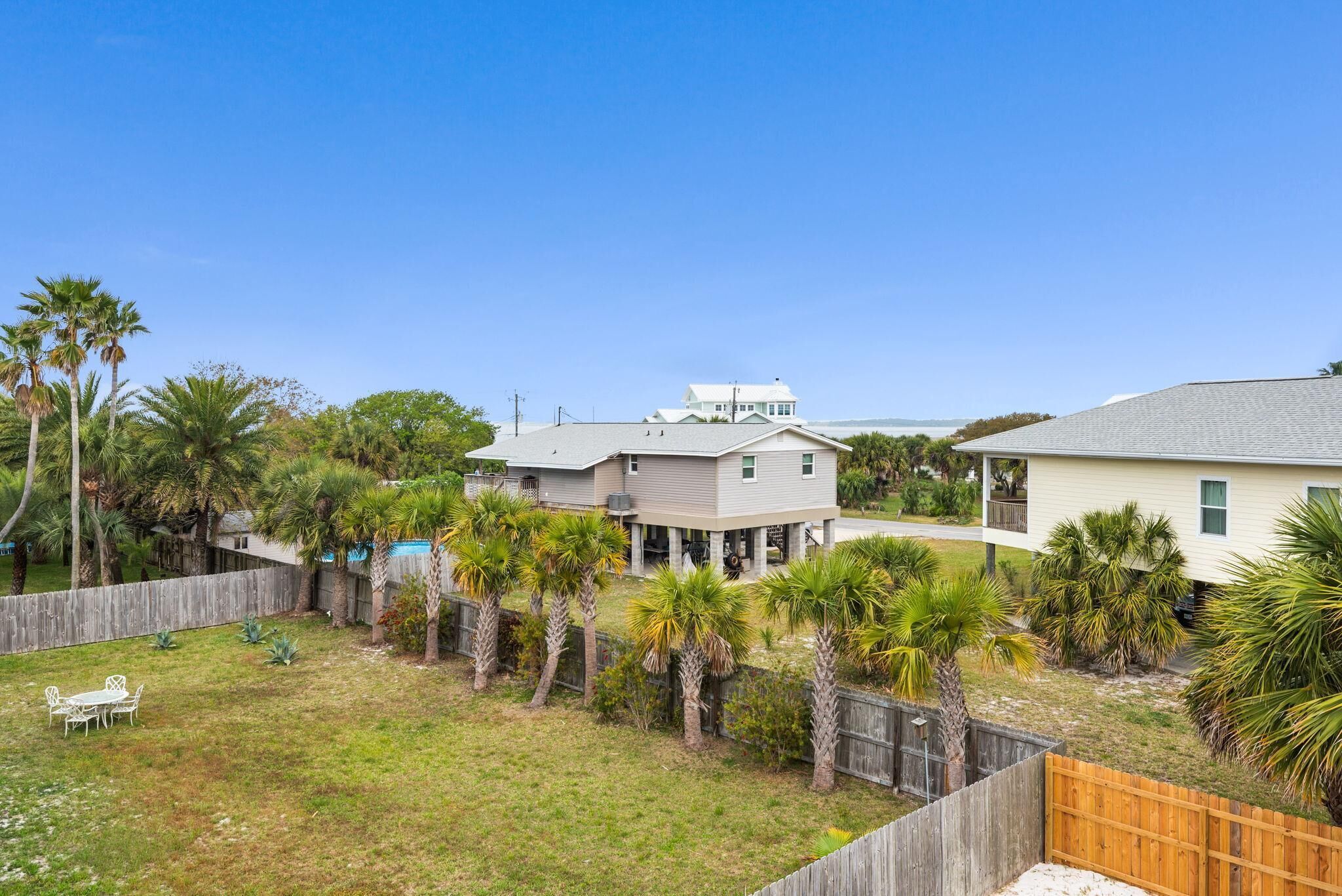 A residential area with a house, a fenced yard, and palm trees.
