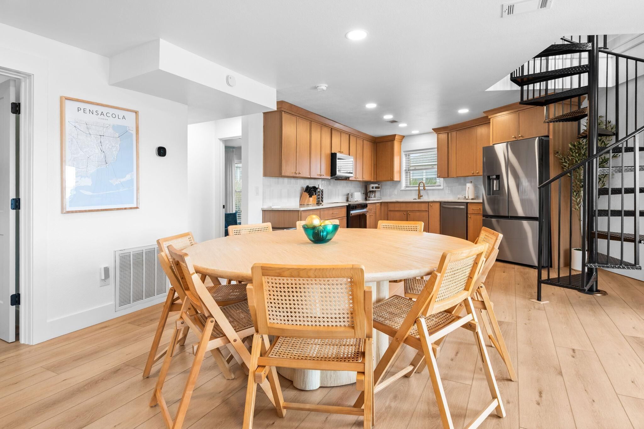 Une cuisine moderne avec des meubles en bois, un îlot central doté de chaises, un réfrigérateur en acier inoxydable et un escalier en colimaçon noir.