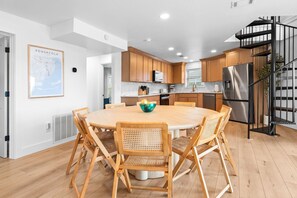 Une cuisine moderne avec des meubles en bois, un îlot central doté de chaises, un réfrigérateur en acier inoxydable et un escalier en colimaçon noir.