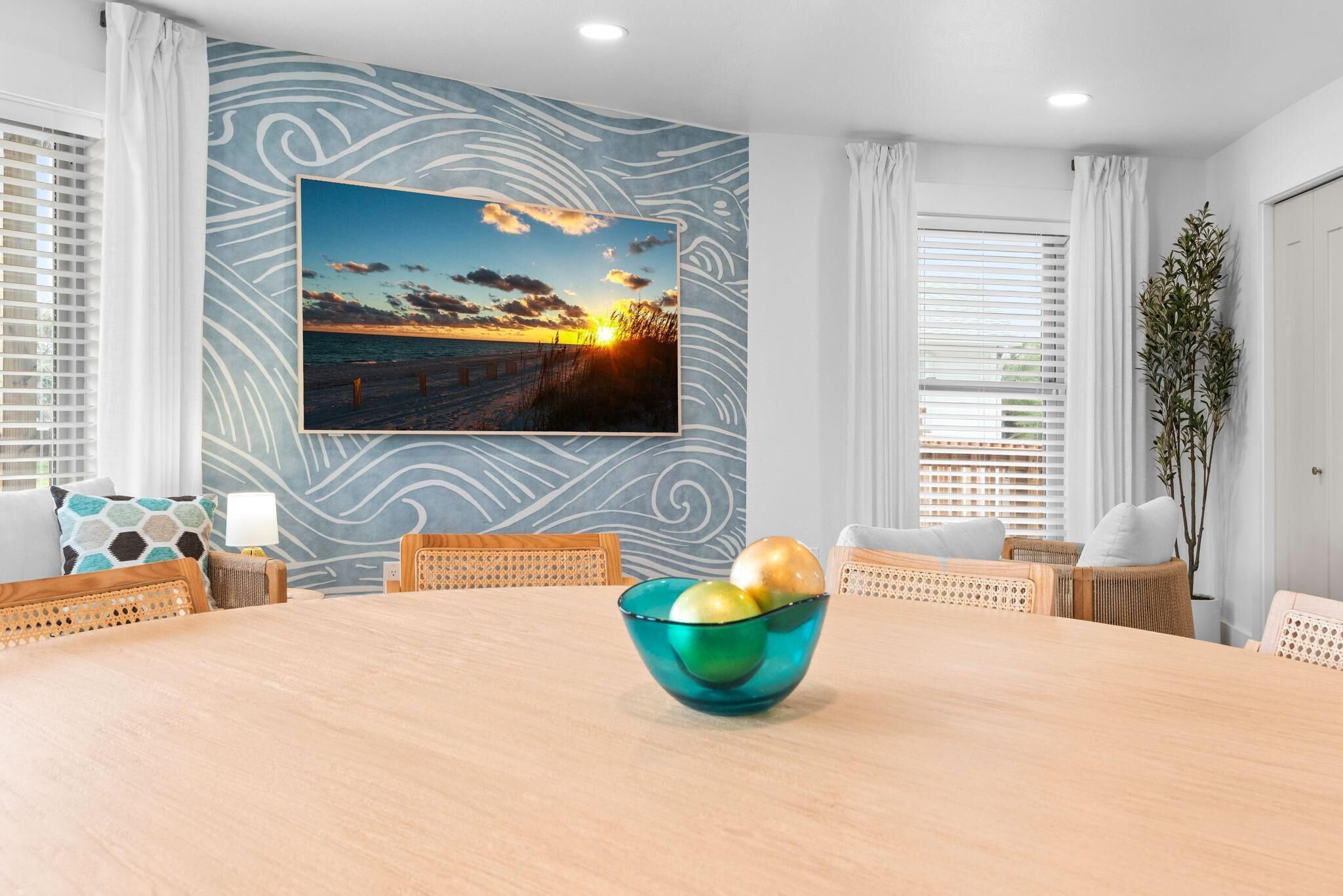 A dining area with a table, chairs, a bowl with fruits, a wall-mounted picture, and a plant.