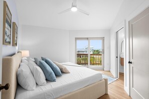 Une chambre avec un lit, un ventilateur de plafond, une vue sur l’extérieur par une porte coulissante et une porte située sur le côté droit.